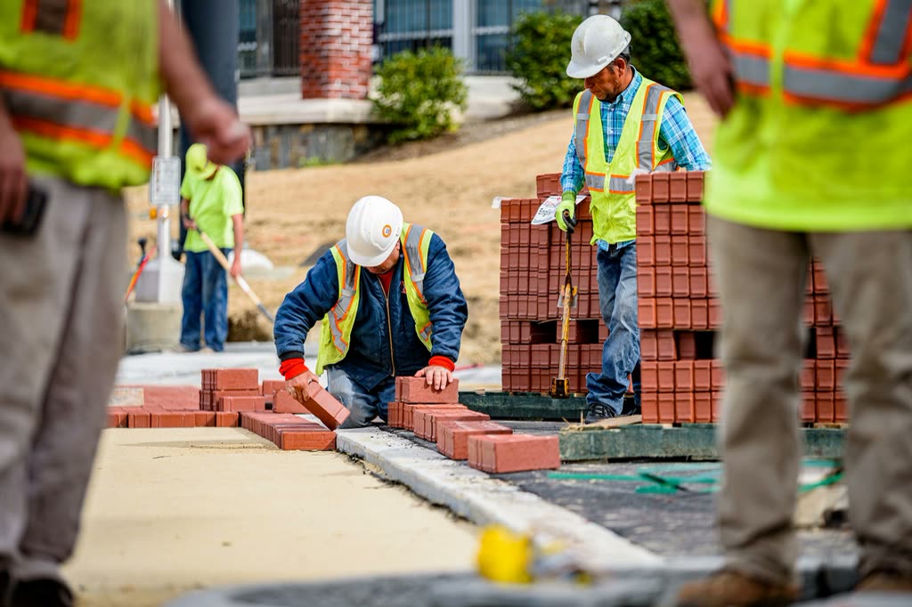 Crew laying brick pavers while a supervisor checks the line
