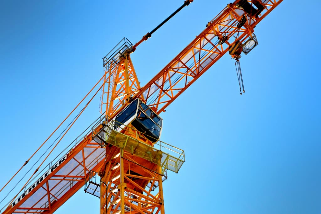 Orange tower crane jib and cab against a clear blue sky