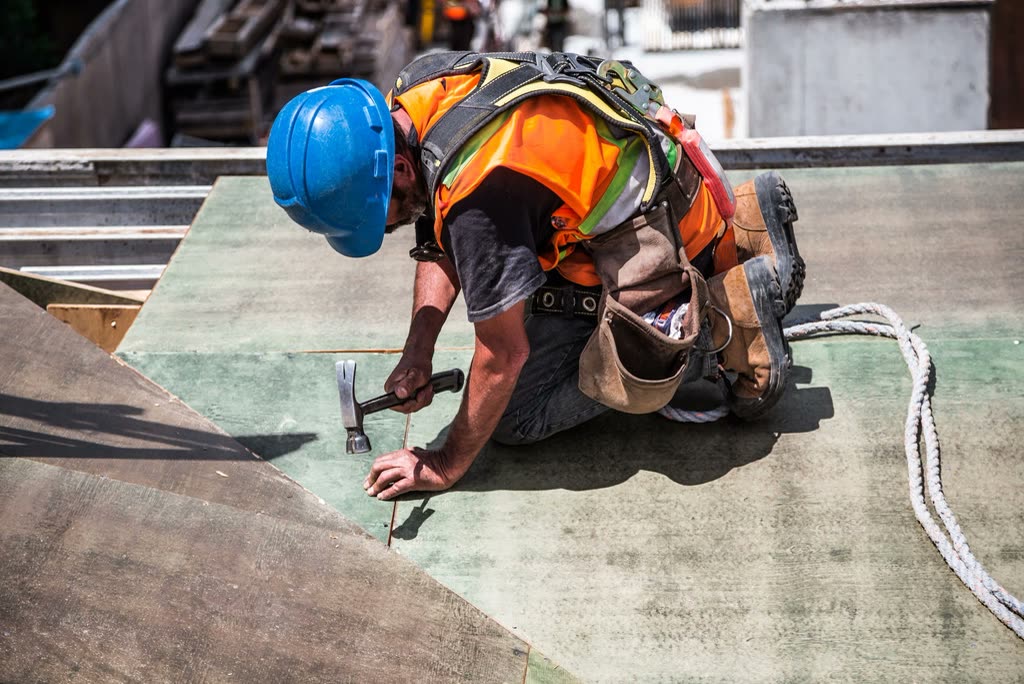 Carpenter in a blue hard hat hammering formwork on a building site